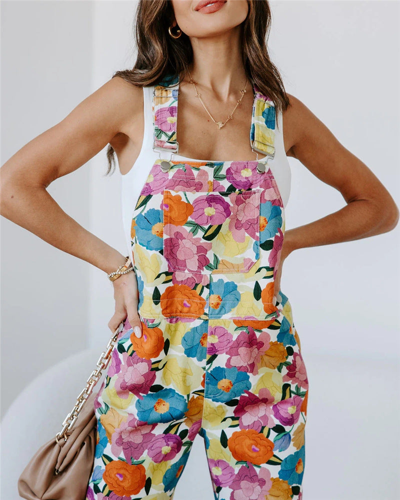 A model wearing a sleeveless, straight-leg floral print jumpsuit in a room with a white background.