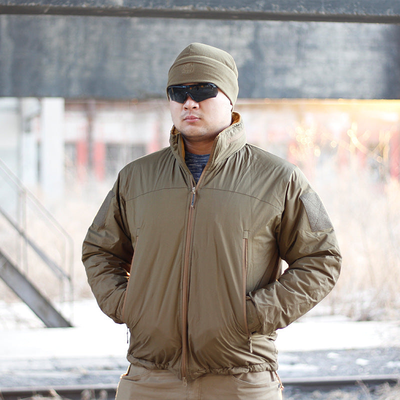 A person wearing a camouflage waterproof coat with a hood, sunglasses, and a beanie. They are standing in a dilapidated building setting.