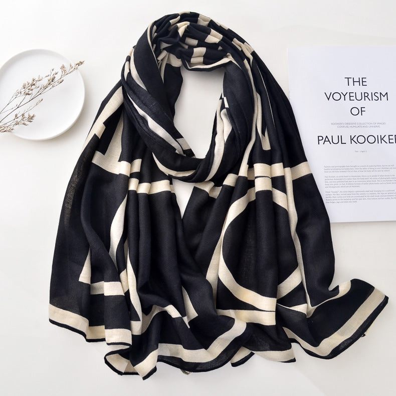 A black pure wool scarf with fringes laid out on a surface, with a photograph and a pearl necklace in the background.