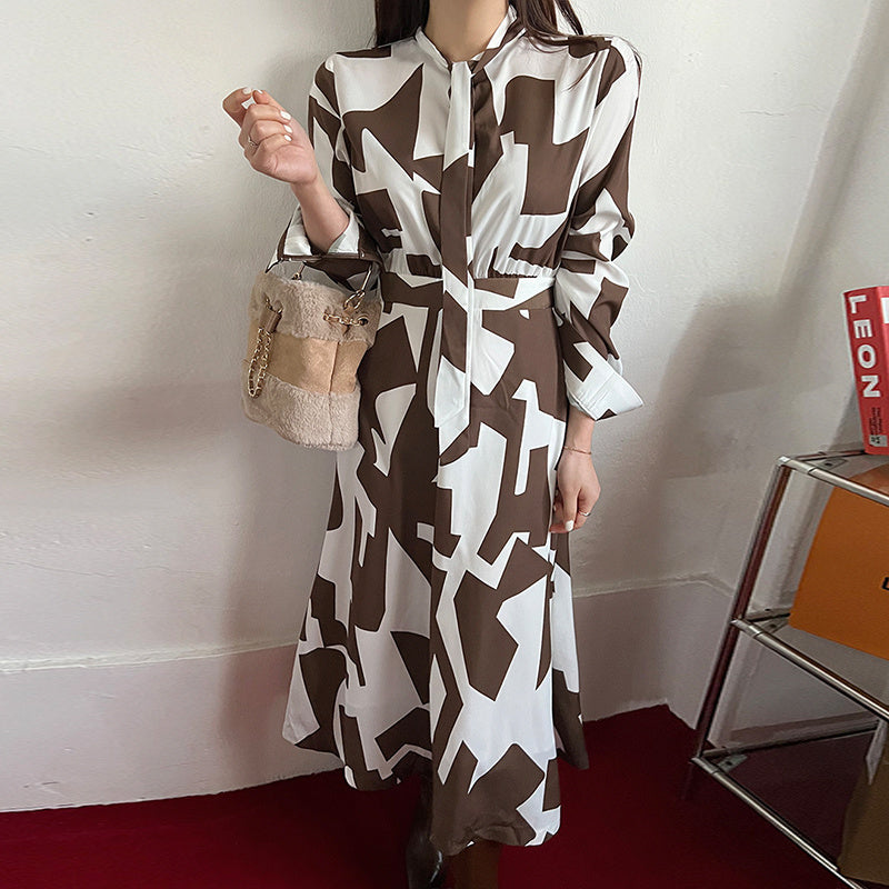 A woman wearing a long sleeve, one-size fit Urban Blossom Print Dress with a round neckline, in black, brown, and white colors, paired with a beige bag and shoes.