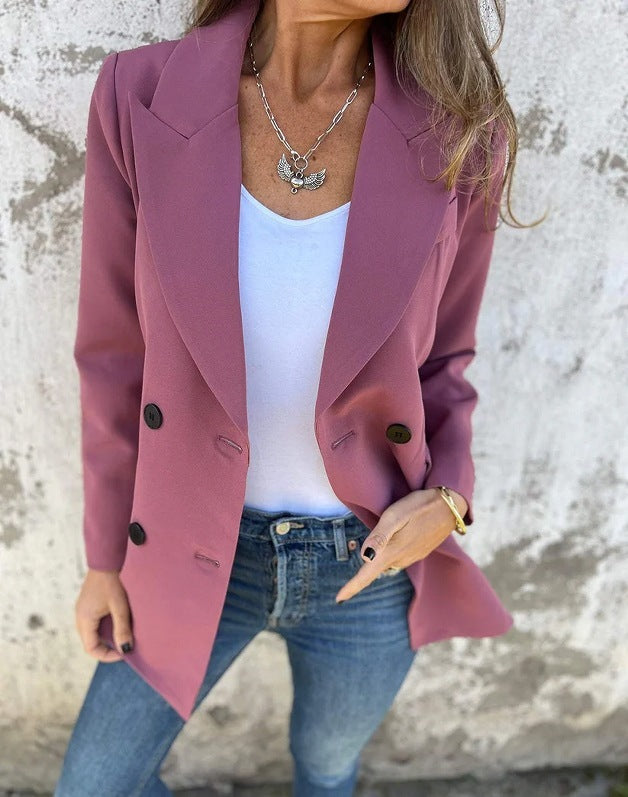 A woman wearing a rose red Urban Grace Lapel Jacket with a white top and blue jeans. She has accessorized with a necklace and has convenient pockets on the jacket.