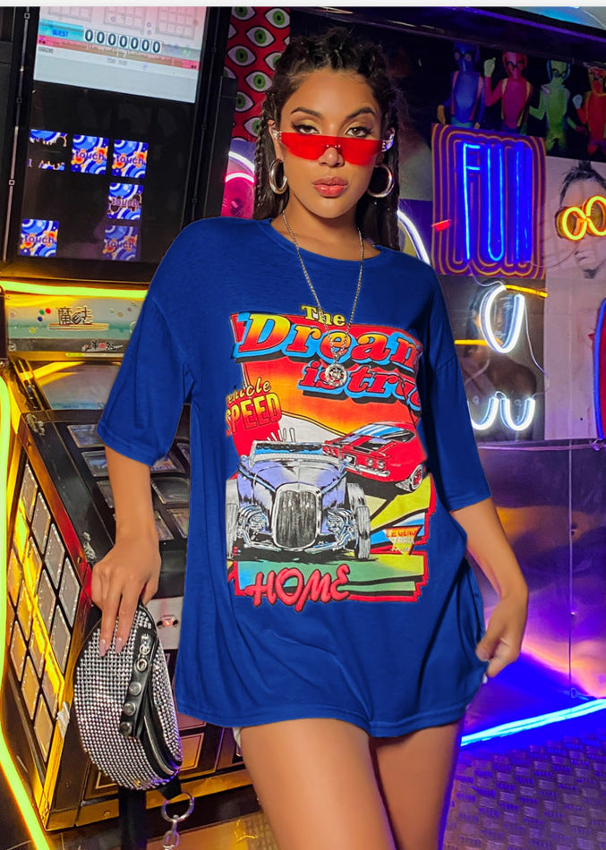 A woman wearing an oversized top with a graphic print, paired with shorts and red sunglasses.