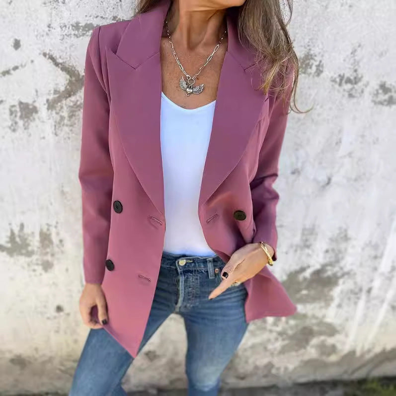 A woman wearing a rose red Urban Grace Lapel Jacket with a white top and blue jeans. She has accessorized with a necklace and has convenient pockets on the jacket.