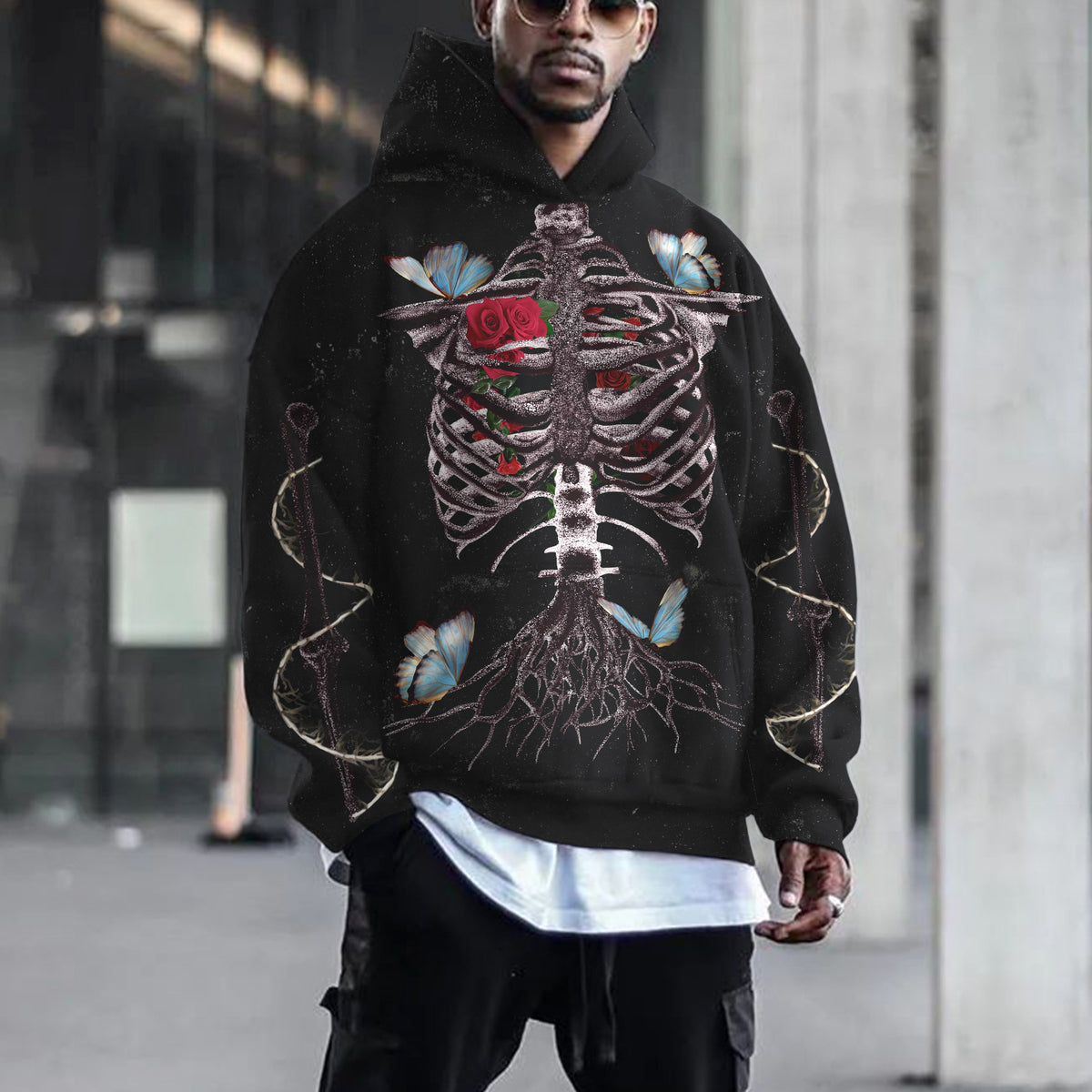 Person wearing a black hoodie with a skeleton design and floral elements outdoors.