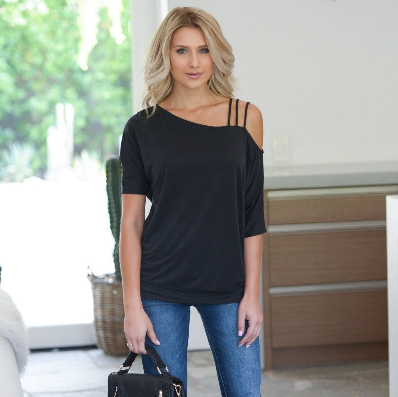 A woman wearing an oversized tee with a round neckline and raglan sleeves, in a black color, paired with blue jeans and carrying a black handbag.