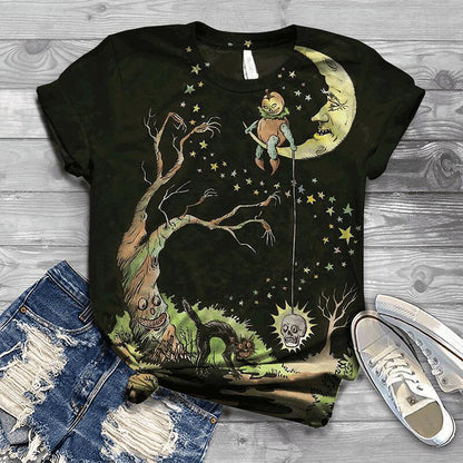 Black t-shirt with a fantasy design featuring a character on a moon, tree, and creature, displayed on a wooden surface with jeans and shoes.