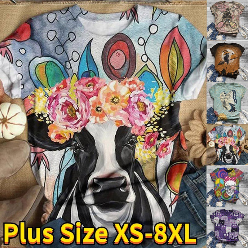 Colorful cow graphic t-shirt with floral headband on a wooden surface, surrounded by more t-shirts.