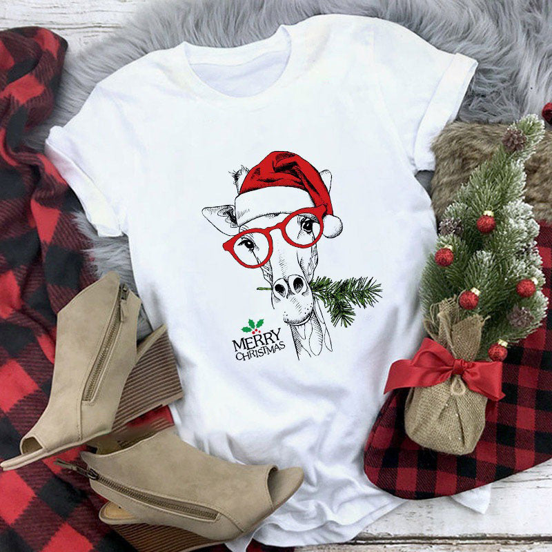 White t-shirt with Christmas-themed design featuring a cow wearing a Santa hat and glasses, surrounded by festive elements on a checkered fabric background.