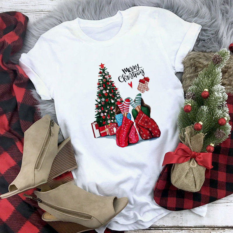 White t-shirt with Christmas-themed design featuring trees, stockings, and boots on a plaid fabric background.