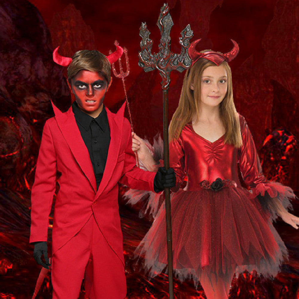 Two children in red devil costumes with horns and a trident against a fiery background.
