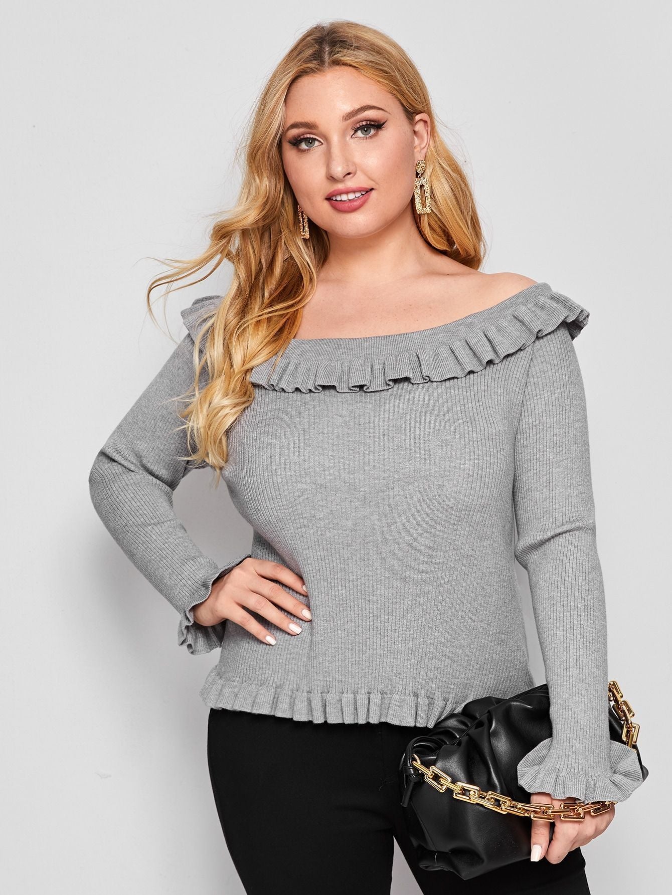 A woman wearing a gray off-shoulder sweater with ruffle detailing and long sleeves.