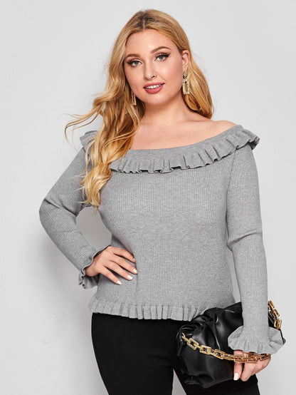 A woman wearing a gray off-shoulder sweater with ruffle detailing and long sleeves.