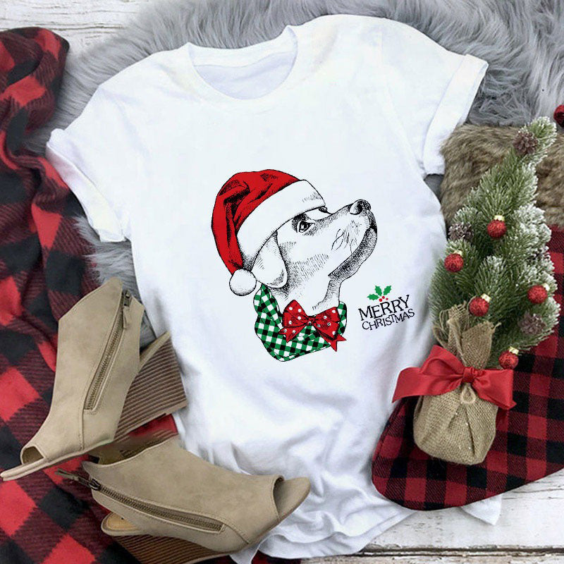 White t-shirt with Christmas-themed design featuring a dog in a Santa hat, surrounded by festive elements on a checkered fabric background.
