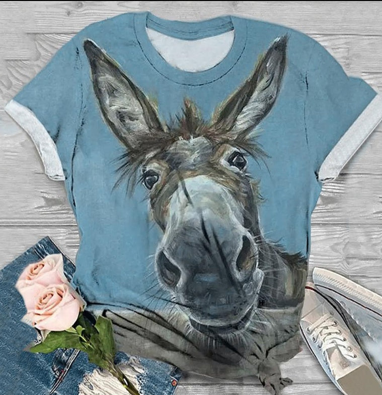 Blue t-shirt with a donkey graphic on a wooden surface with flowers and shoes.