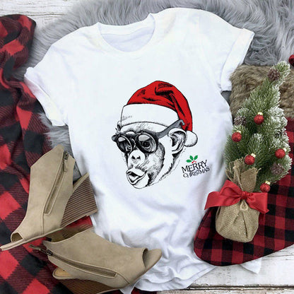White t-shirt with a monkey wearing a Santa hat and Christmas tree design, placed on a checkered fabric with boots and a stocking.