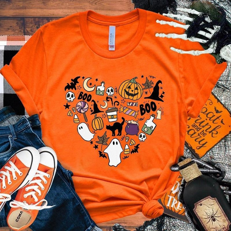 Orange t-shirt with Halloween-themed graphics on a wooden surface with accessories.